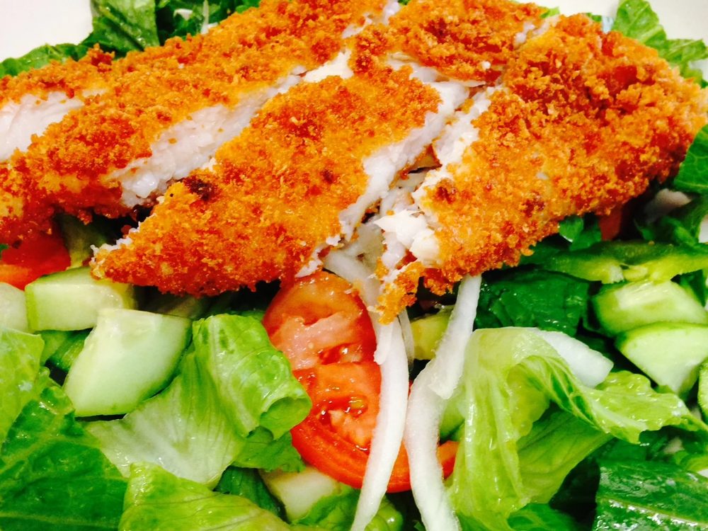 A crispy fried chicken breast sliced over a garden salad with tomato and cucumber