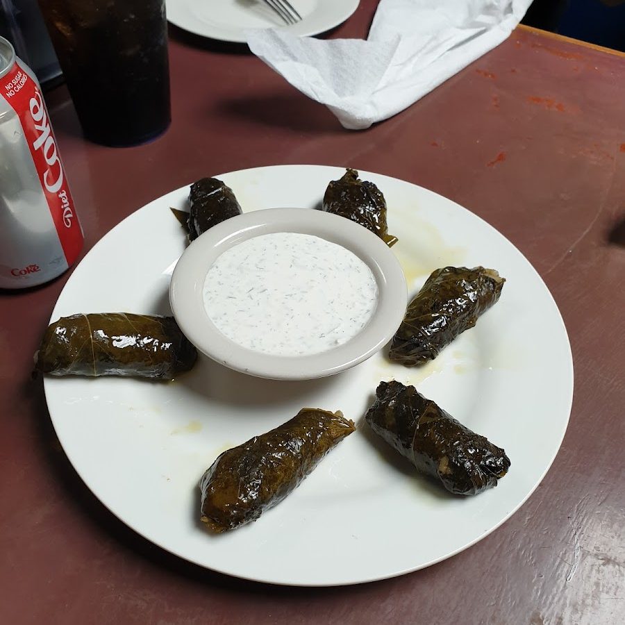 Six dolmades, stuffed grape leaves, plated around a bowl of tzatziki sauce