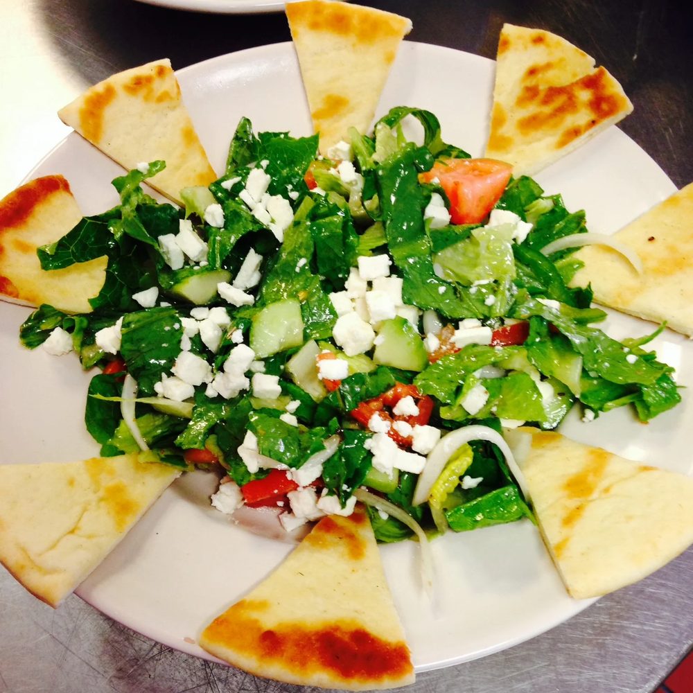 A Greek salad with feta cheese, surrounded by wedges of toasted pita bread