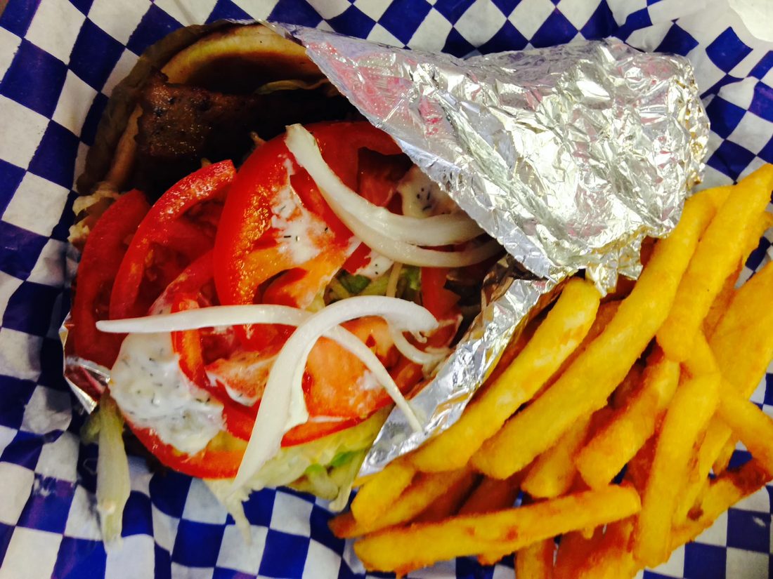 A traditional lamb gyro wrapped in foil, served with french fries in a blue checkered basket