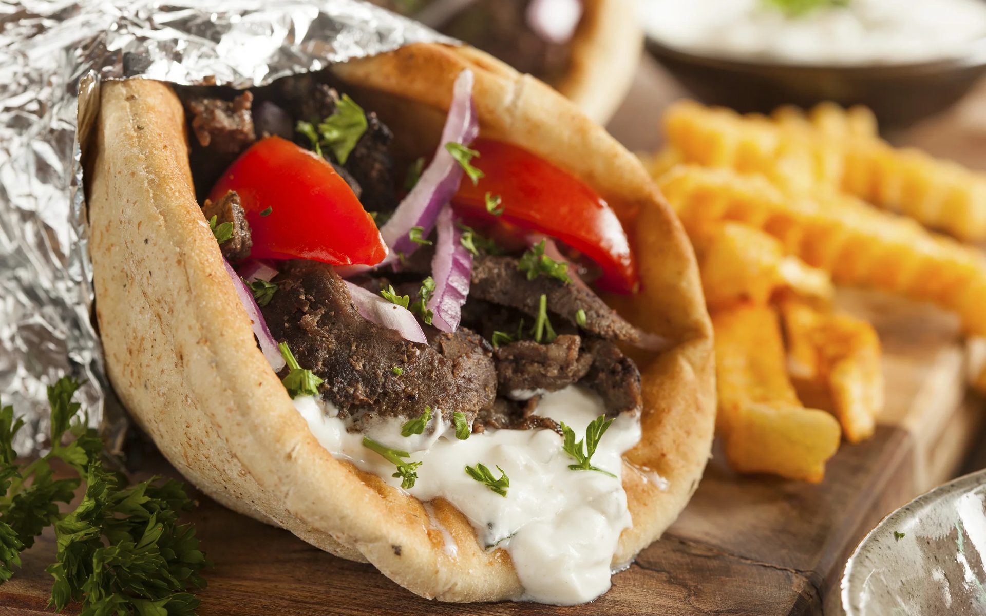 A lamb gyro in warm pita with tomato, red onion and tzatziki, next to crinkle-cut fries